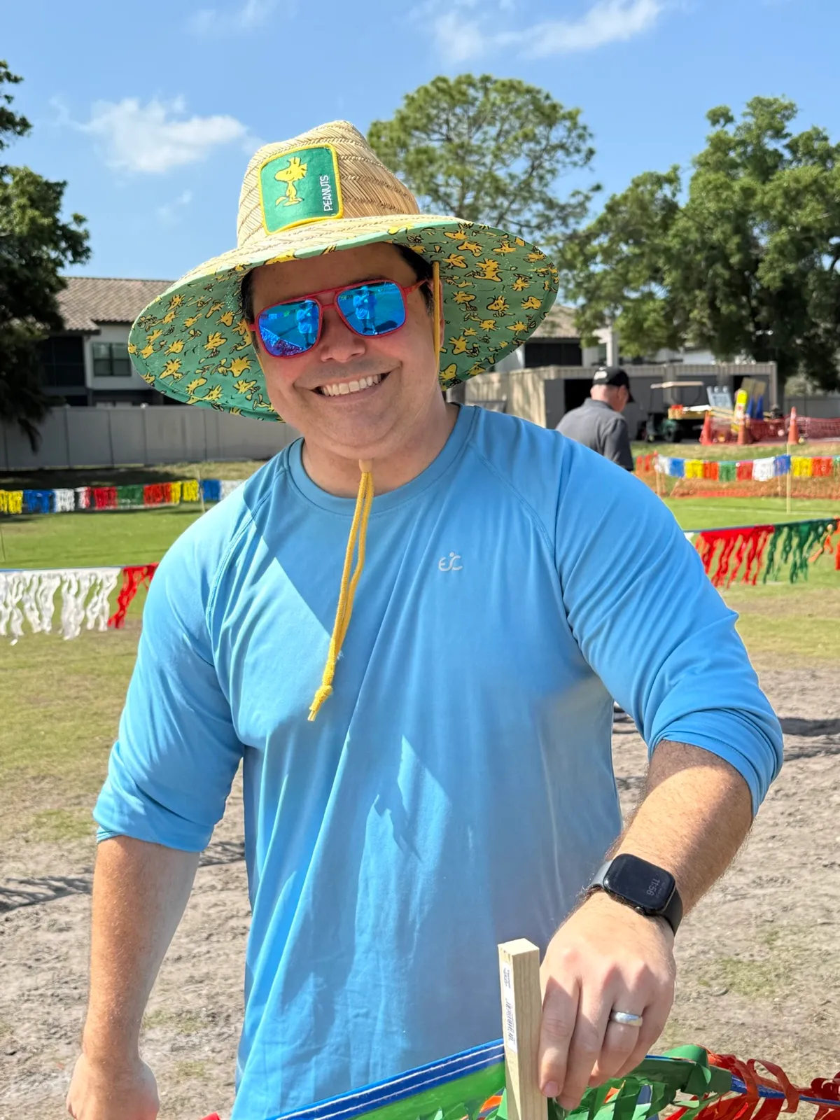 A smiling volunteer in a decorated hat at an outdoor church festival